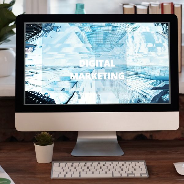 A desktop computer screen on an office desk displays the words digital marketing